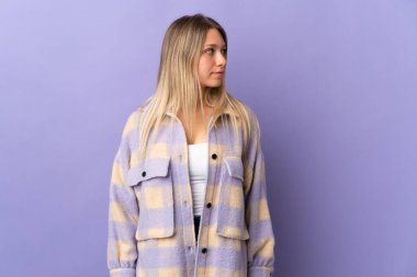 Mor arka planda izole edilmiş genç sarışın kadın yan tarafa bakıyor.