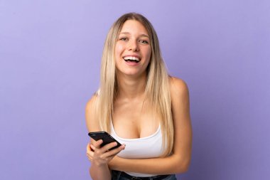 Mor arka planda izole edilmiş cep telefonu kullanan genç sarışın kadın gülüyor.