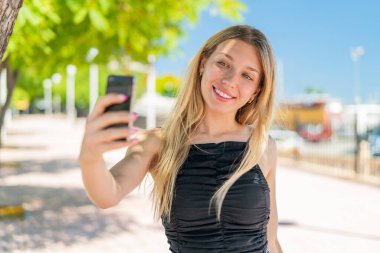 Açık havada genç sarışın bir kadın selfie çekiyor.
