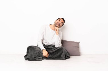 Kafkasyalı pijamalı bir adam yerde oturuyor ve yukarı bakıyor.