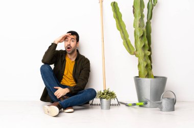 Bahçıvan içeride yerde oturuyor. Yan tarafa bakarken sürpriz jest yapıyor.