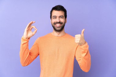 İzole edilmiş mor arka planda beyaz yakışıklı bir adam işaret ve baş parmak hareketi gösteriyor.