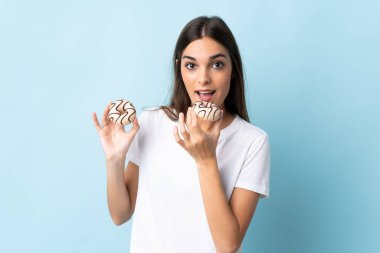 Mavi arka planda izole edilmiş genç beyaz kadın donut yiyor.