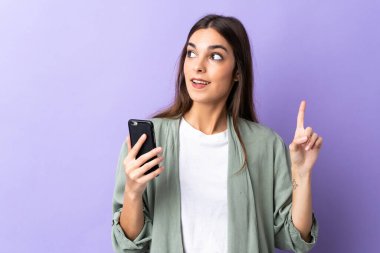 Mor arka planda izole edilmiş cep telefonu kullanan beyaz bir kadın çözümü bulmak için parmağını kaldırıyor.
