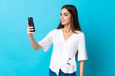 Mavi arka planda izole edilmiş beyaz bir kadın selfie çekiyor.