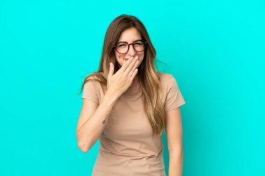 Mavi arka planda izole edilmiş genç beyaz kadın mutlu ve gülümsüyor.