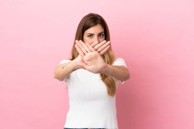 Pembe arka planda izole edilmiş beyaz bir kadın bir eylemi durdurmak için elleriyle dur hareketi yapıyor.