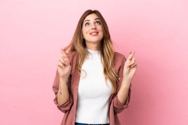 Pembe arka planda izole edilmiş beyaz bir kadın parmaklarını çapraz yapıp en iyisini diliyor.