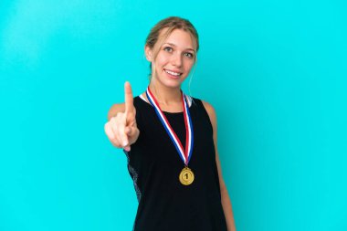 Mavi arka planda madalyalı genç beyaz kadın parmağını kaldırıyor ve gösteriyor.