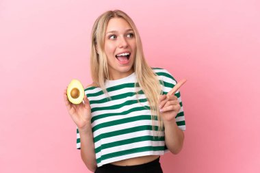 Pembe arka planda avokado tutan beyaz bir kadın çözümü bulmak için parmağını kaldırıyor.