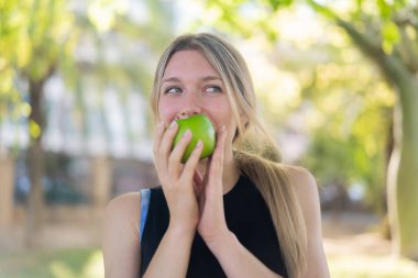 Açık havada, elinde elma tutan genç sarışın kadın.