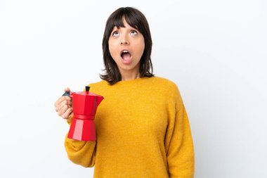 Beyaz arka planda kahve demliği tutan genç bir ırk kadını şaşırmış bir ifadeyle yukarı bakıyor.