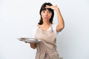 Tepsisi beyaz arka planda olan genç garson yan tarafa bakarken sürpriz jest yapıyor.