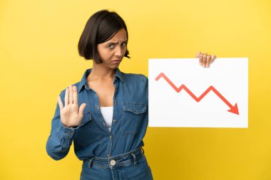 Sarı arka planda izole edilmiş genç bir ırk kadını elinde azalan bir istatistik ok sembolü olan bir tabela tutuyor ve dur işareti yapıyor.