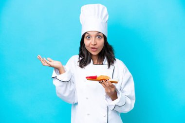 Genç İspanyol aşçı kadın elinde saşimi tutarken mavi arka planda şok olmuş yüz ifadesi ile izole edilmiş.