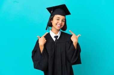 Üniversiteden mezun genç bir kız izole edilmiş mavi bir geçmişle baş parmak işareti yapıyor.
