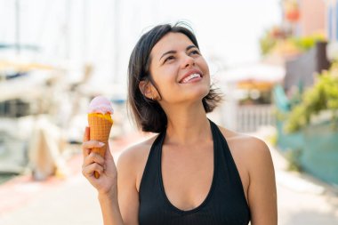 Açık havada kornet dondurması olan genç, güzel Bulgar kadın gülümserken yukarı bakıyor.