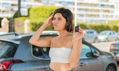 Genç, güzel, Bulgar bir kadın araba anahtarlarını açık havada tutuyor. Şüpheleri var ve kafası karışık bir ifadeyle bakıyor.