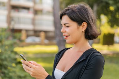 Genç, güzel Bulgar kadın açık havada cep telefonuyla mesaj ya da e-posta gönderiyor.
