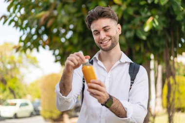 Genç yakışıklı adam dışarıda portakal suyu tutuyor.