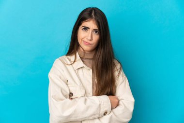 Mavi arka planda izole edilmiş genç beyaz kadın üzgün hissediyor.