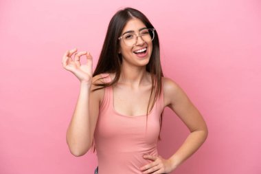 Pembe arka planda izole edilmiş beyaz bir kadın parmaklarıyla tamam işareti gösteriyor.