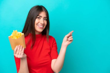 Genç beyaz kadın patates kızartması yakalıyor. Mavi arka planda izole edilmiş.