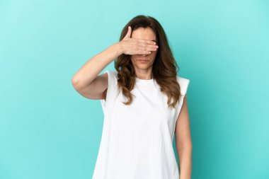 Orta yaşlı, beyaz bir kadın mavi arka planda tek başına, gözleri elle kapatıyor. Bir şey görmek istemiyorum.