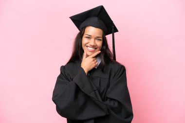 Kolombiyalı genç bir üniversite mezunu pembe arka planda izole edilmiş gülümsüyor.