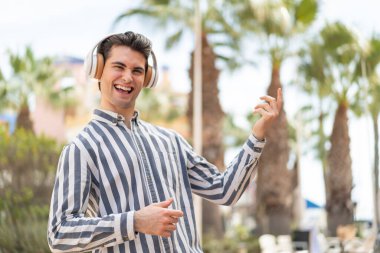 Genç yakışıklı adam müzik dinliyor ve gitar hareketi yapıyor.