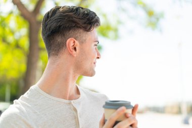 Elinde kahve tutan yakışıklı bir delikanlı.