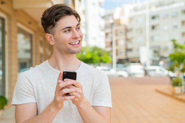 Genç ve yakışıklı bir adam cep telefonu kullanıyor.