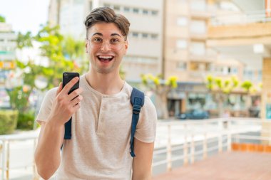 Dışarıda cep telefonu kullanan yakışıklı bir genç. Şaşırmış ve şok olmuş bir yüz ifadesi var.