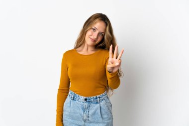 Mavi arka planda izole edilmiş genç sarışın kadın mutlu ve parmaklarıyla üçe kadar sayıyor.