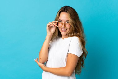 Mavi arka planda gözlüklü ve mutlu genç sarışın kadın.
