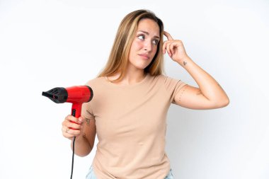 Beyaz arka planda izole edilmiş saç kurutma makinesini tutan beyaz saçlı genç bir kadın. Şüpheleri var ve kafası karışık.