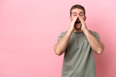 Pembe arka planda izole edilmiş genç beyaz adam bağırıyor ve bir şey duyuruyor.