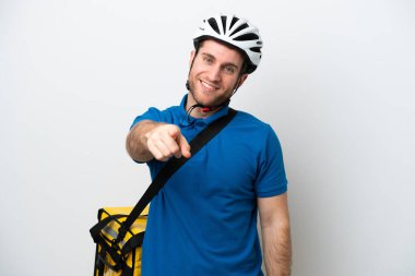 Beyaz arka planda izole edilmiş termal sırt çantalı beyaz tenli genç beyaz adam kendine güvenen bir ifadeyle sana parmak basıyor.