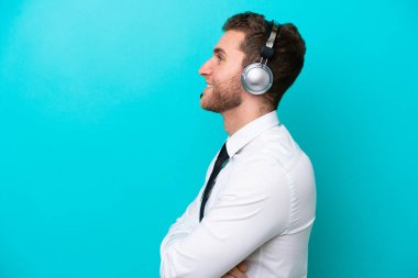 Tele pazarlamacı beyaz adam mavi arka planda mavi bir kulaklıkla çalışıyor.