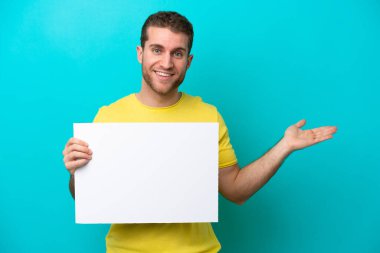 Kafkasyalı genç adam mavi arka planda izole edilmiş. Elinde şaşırmış bir ifadeyle boş bir levha var.