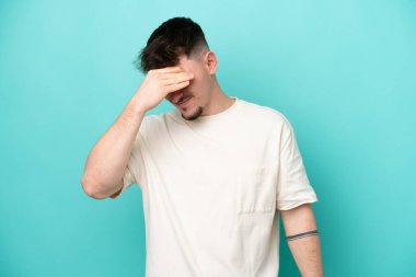 Kafkasyalı yakışıklı genç adam mavi arka planda başağrısı ile izole edilmiş.