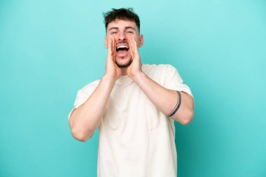 Beyaz tenli yakışıklı adam mavi arka planda izole edilmiş bağırıyor ve bir şeyler söylüyor.