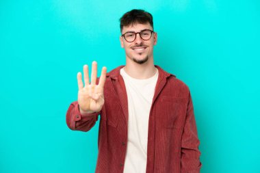 Genç, beyaz, yakışıklı bir adam mavi arka planda izole edilmiş mutlu ve parmaklarıyla dört kişi sayıyor.