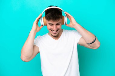 Genç beyaz yakışıklı adam mavi arka planda izole edilmiş müzik dinliyor.