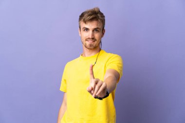 Mor arka planda izole edilmiş genç sarışın adam parmağını kaldırıyor ve gösteriyor.