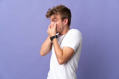Genç yakışıklı sarışın adam mor arka planda izole edilmiş ağzını kapatıyor ve yan tarafa bakıyor.