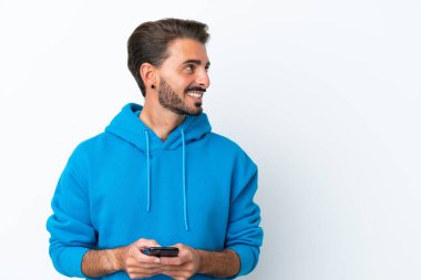Beyaz arka planda izole genç beyaz adam cep telefonu kullanarak ve yukarı bakarak