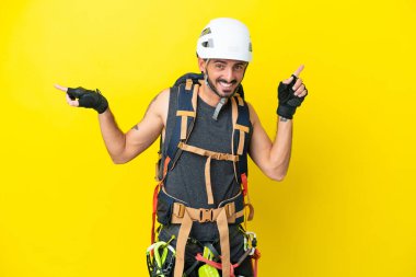 Kafkasyalı genç dağcı sarı arka planda izole edilmiş, parmak uçlarını işaret ediyor ve mutlu.