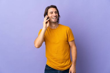 Mor arka planda izole edilmiş genç bir adam cep telefonuyla sohbet ediyor.