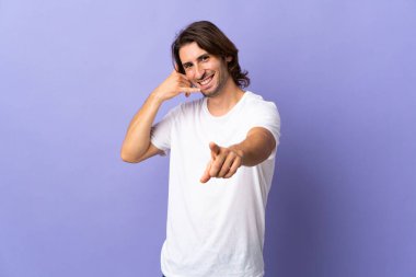 Mor arka planda izole edilmiş genç yakışıklı bir adam telefon hareketi yapıyor ve ön tarafı işaret ediyor.